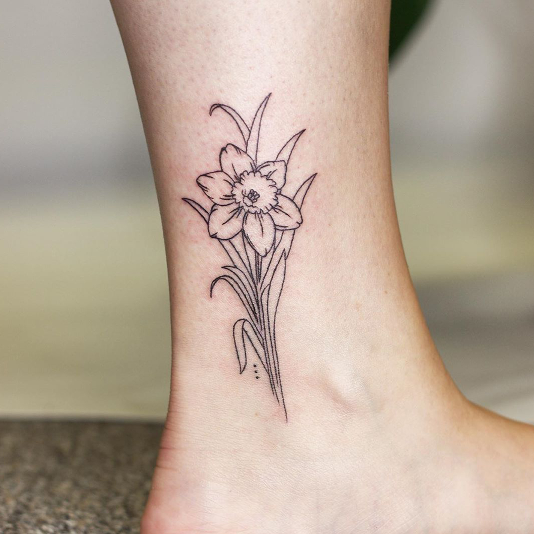 Minimalist daffodil tattoo on the ankle.
